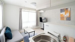 Una camera d'albergo moderna con un divano, un tavolino, un angolo cottura con lavandino e una TV.