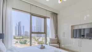 A modern hotel room with a large bed, a TV, and a view of a cityscape through floor-to-ceiling windows. - Downtown Views Residences - Downtown DXB (Dubai)
