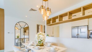 A modern dining area with a white table set for four, surrounded by grey chairs. A vase of white flowers is on the table, and there is a kitchen area with a stainless steel refrigerator in the background. - Downtown Views Residences - Downtown DXB (Dubai)