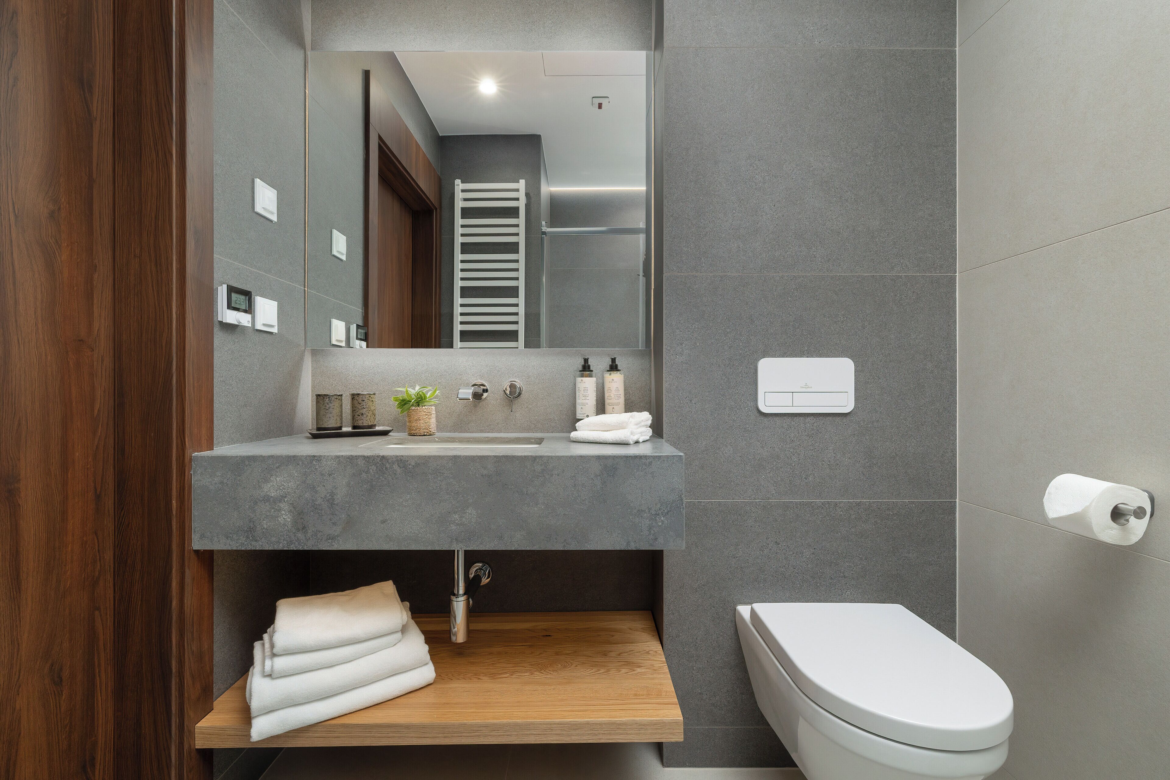 A modern bathroom with a wooden vanity, a toilet, and a large mirror.