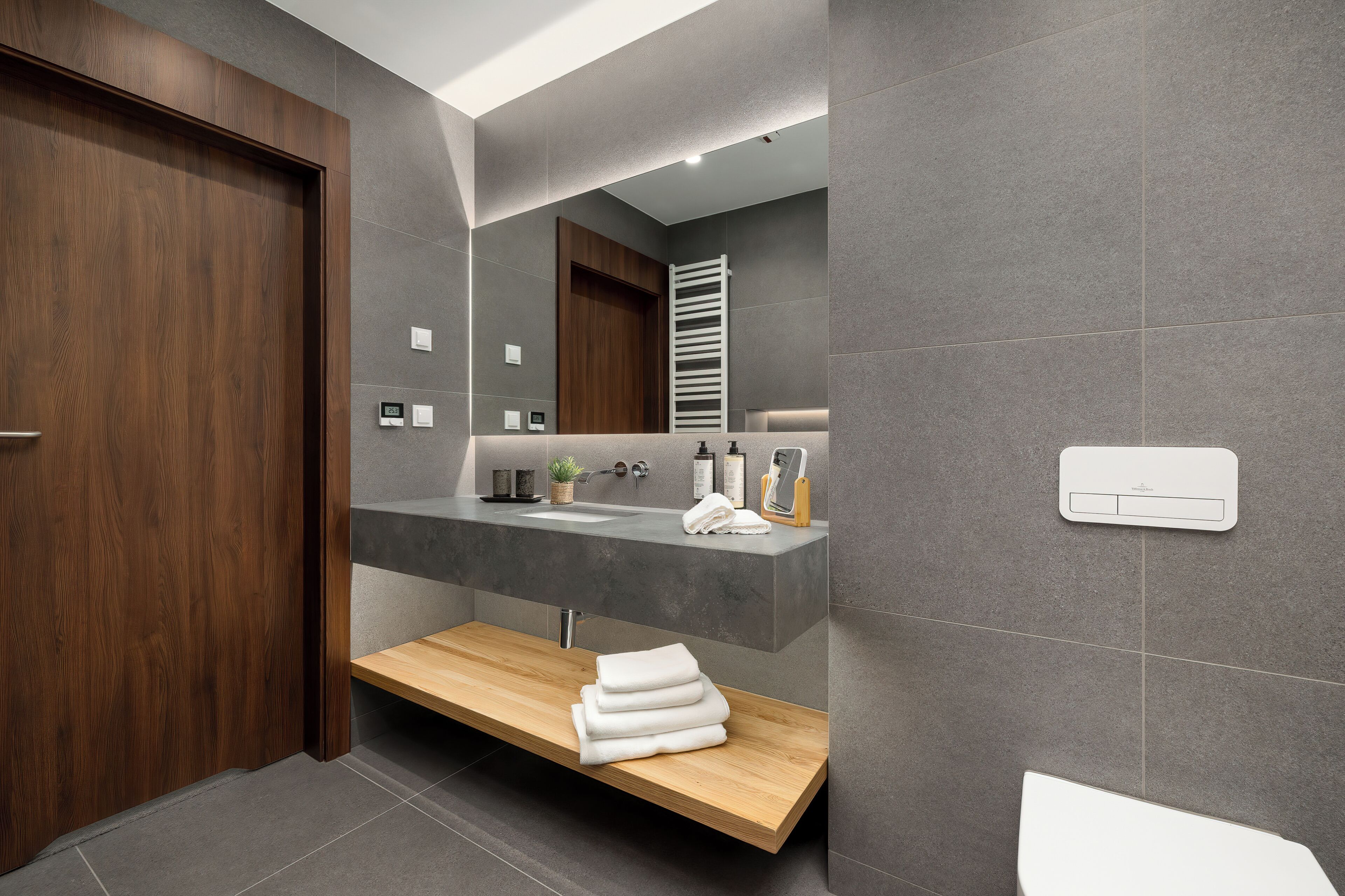 A modern bathroom with a wooden door, a built-in sink, a towel rack, and a mirror.