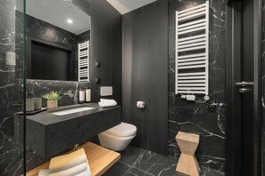 A modern bathroom with a dark marble wall, a wooden vanity, a white toilet, and a towel rack. - West Baltic City (Szczecin)