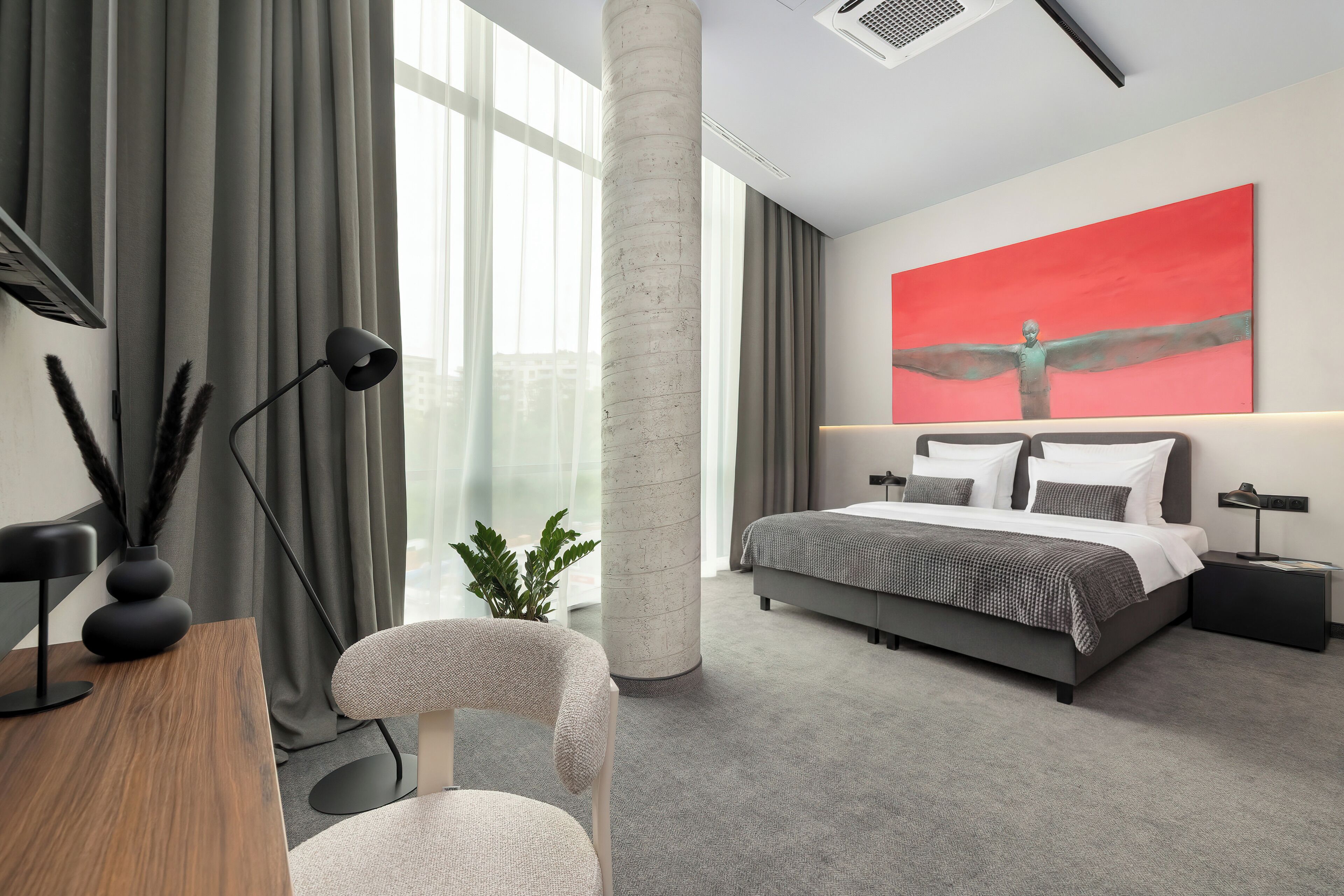 A modern bedroom with a large bed, a desk, a chair, a plant, and a large window.
