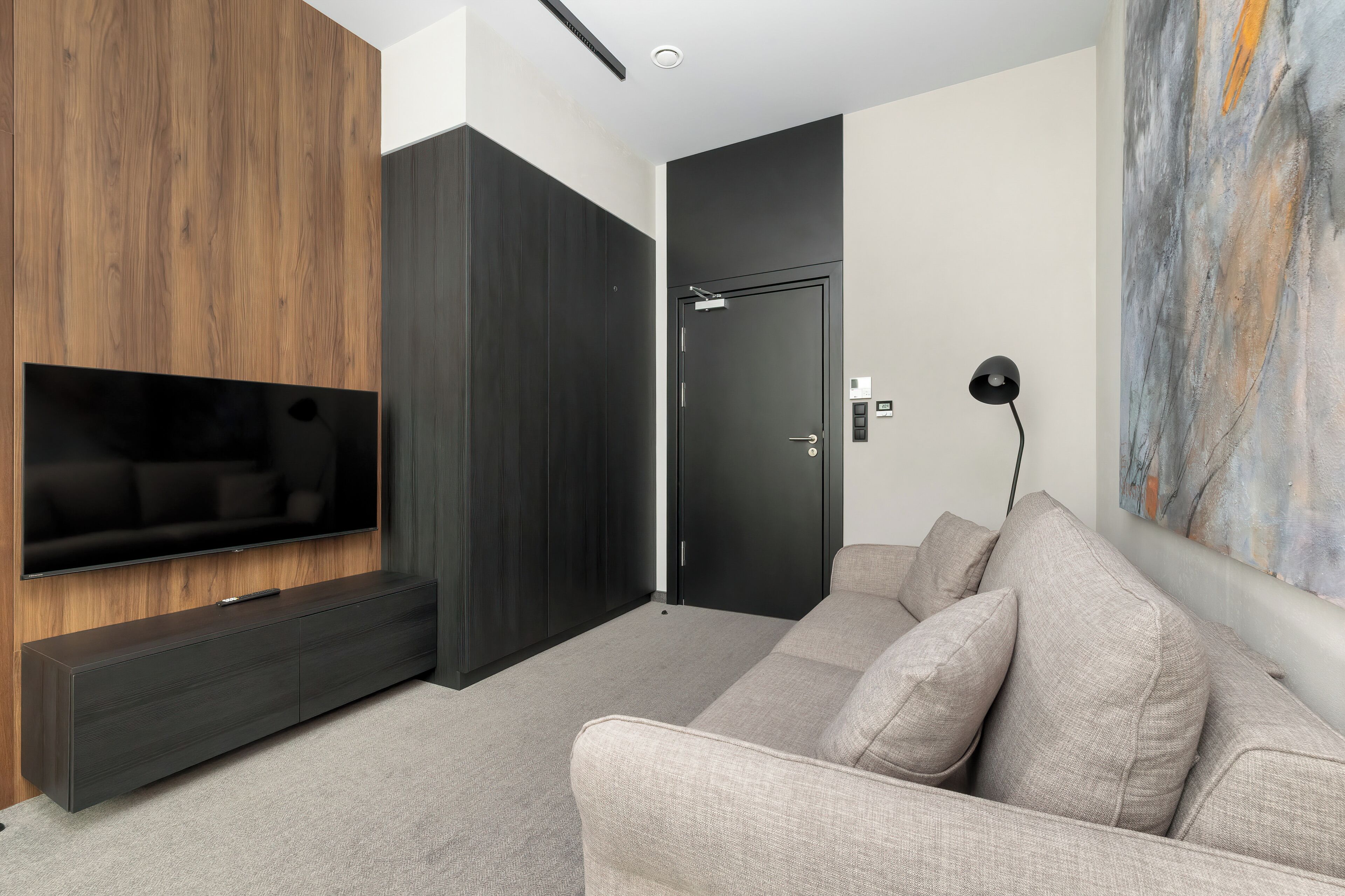 A modern living room with a flat-screen TV, dark wood and black wardrobe, a grey sofa, and a painting on the wall.
