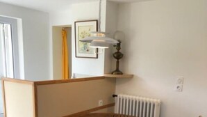 A room with a round wooden table and four chairs, a radiator, a wall-mounted lamp, and a framed picture. - Charming country studio (Dolmayrac)