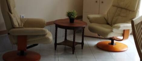 A living room with two beige armchairs, a small round table with a plant, and a cabinet.