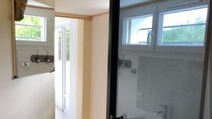 A modern bathroom with a glass shower enclosure, a white sink, and a window above the mirror. - Charming country studio (Dolmayrac)