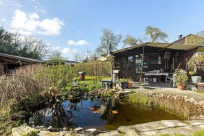 Un espacio exterior rústico con un estanque, construcciones de madera y un edificio con techo inclinado.