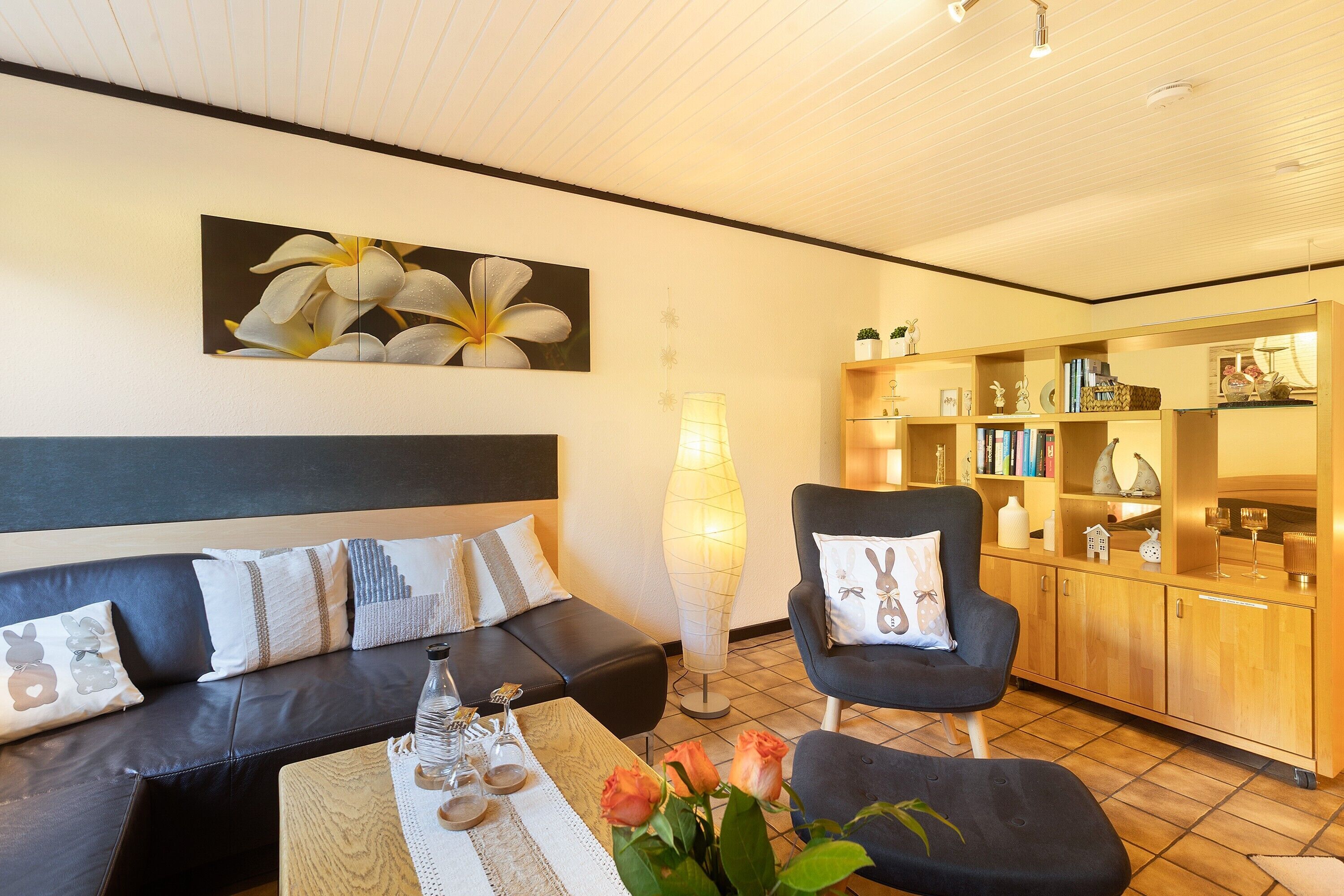Una sala de estar moderna con un sofá, un sillón y una mesa de centro, una estantería y un cuadro grande de flores en la pared.
