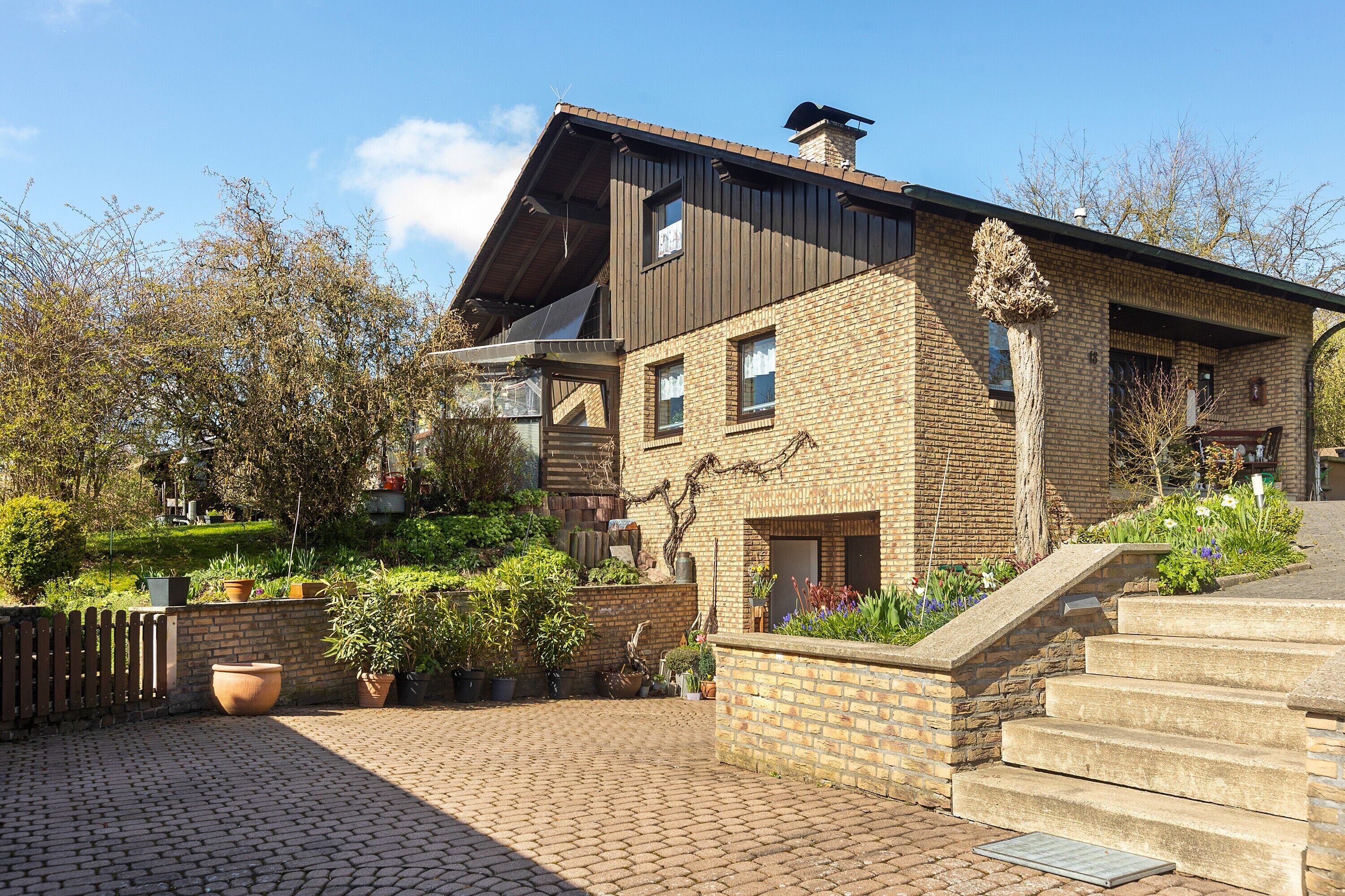 Een huis met twee verdiepingen, een bakstenen gevel, een houten terras en een trap naar de ingang.