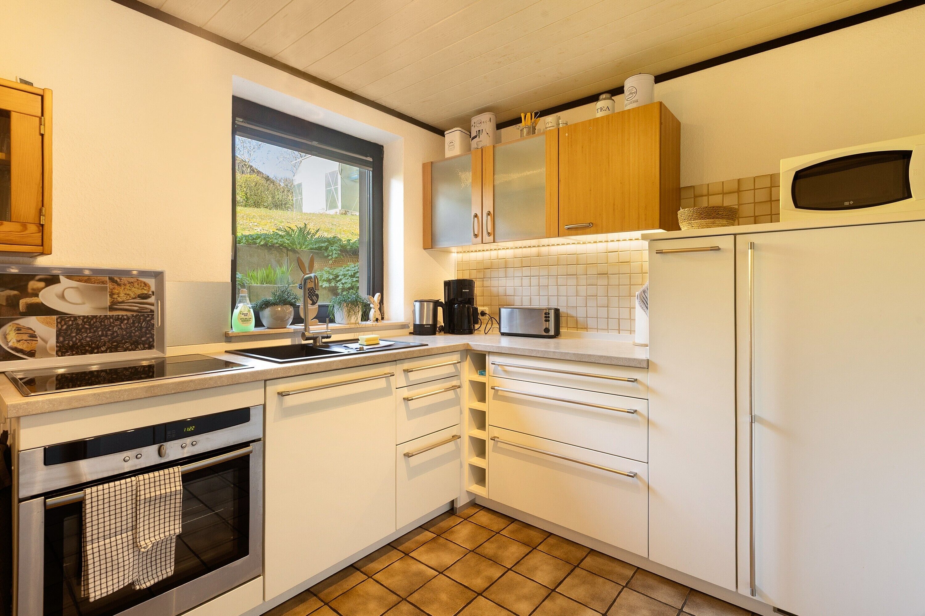 A modern kitchen with white cabinetry, a built-in oven, a microwave, and a window providing a view of the outdoors.