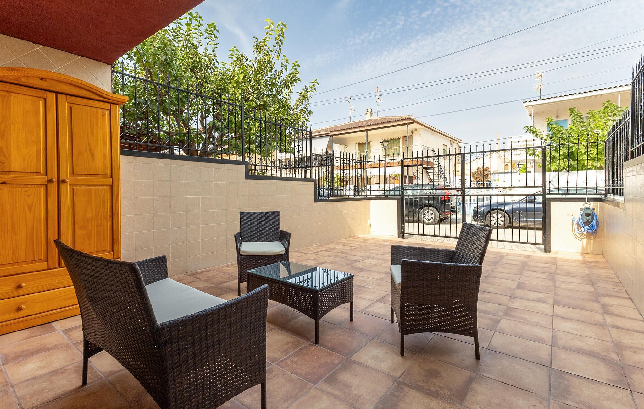 Un patio al aire libre con muebles de mimbre, piso de baldosas y vista a una calle residencial.