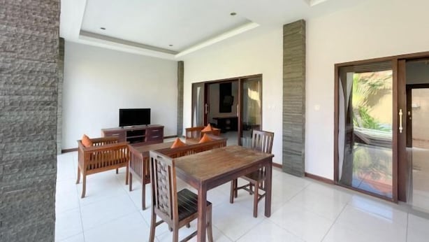 A spacious room with a wooden dining table and chairs, a flat-screen TV, and a sliding glass door leading to an outdoor area. - The Lavana Bali Radiance Arjuna Villa Seminyak (Bali)