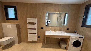A modern bathroom with a toilet, a sink with a mirror, and a washing machine. - Lodging in a garden near Fraispertuis City Park. (Rambervillers)