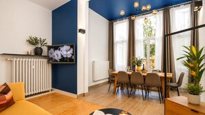 A modern living room with a sofa, a dining table with chairs, a TV on the wall, and a window with curtains. - Wohnung mit schoenem Garten (Bielefeld)