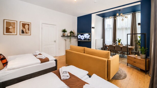 Habitación de hotel con dos camas, un sofá, zona de comedor y televisión.