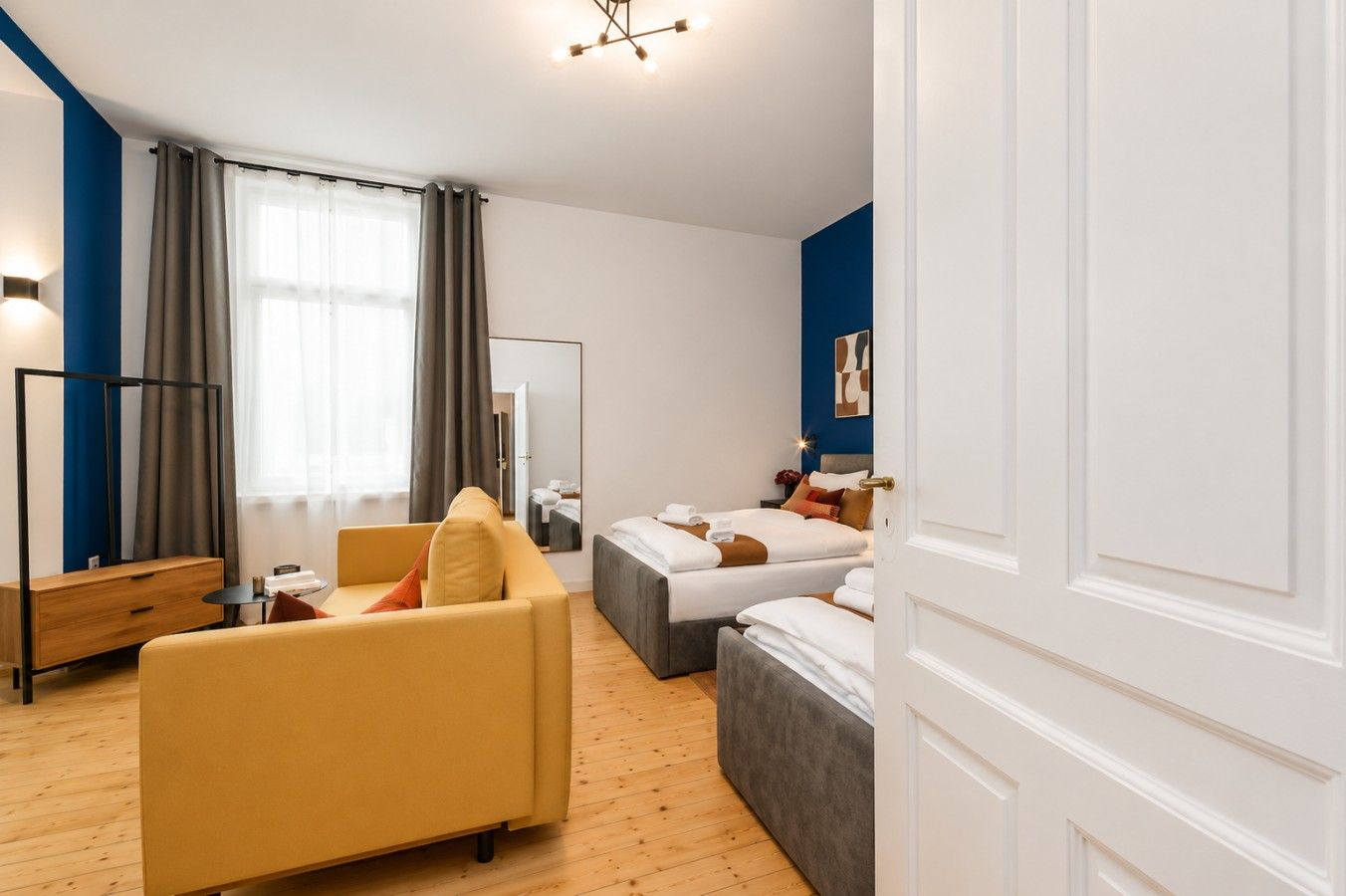 Ein Hotelzimmer mit einer Couch, zwei Betten, einem Spiegel, einem Nachttisch und einem Kleiderschrank.