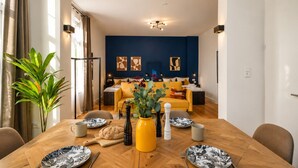 Un comedor con una mesa de madera dispuesta para dos personas, una planta en maceta y un jarrón amarillo.