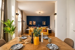 Un comedor con una mesa de madera dispuesta para dos personas, una planta en maceta y un jarrón amarillo.