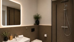 Un baño moderno con un espejo grande, un lavamanos, un inodoro y una ducha.