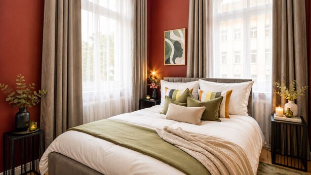 A bedroom with a large bed, a bedside table, a nightstand, a window with curtains, and a painting on the wall. - 2-Bett-Wohnung mit Eigener Küche & Waschküche (Bielefeld)