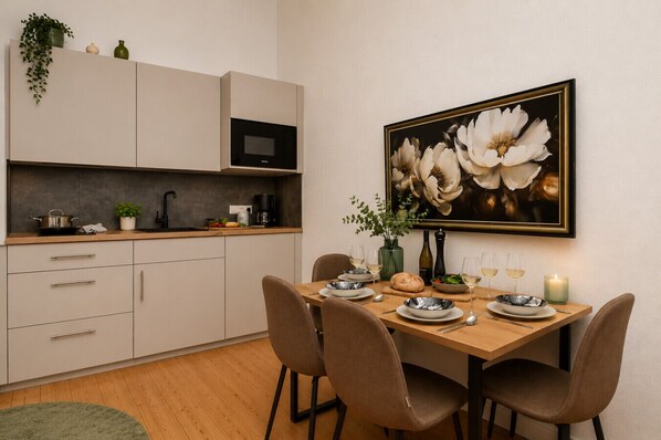 Uma cozinha moderna com área de jantar, com armários, micro-ondas, mesa para dois e um quadro grande com flores na parede.
