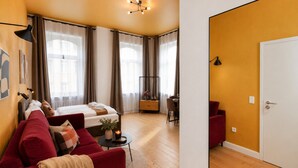 Una habitación de hotel moderna con cama, sofá rojo, zona de comedor y una puerta blanca.