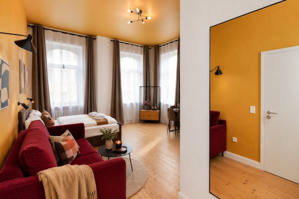 A modern hotel room with a bed, red sofa, dining area, and a white door. - Zentrales Studio mit Küche & Waschküche (Bielefeld)