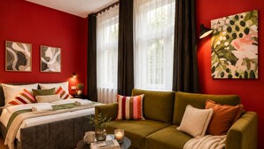 A bedroom with a bed, a green sofa, a coffee table, and artwork on the walls. - Helles Studio mit Waschküche – Paulusstraße (Bielefeld)
