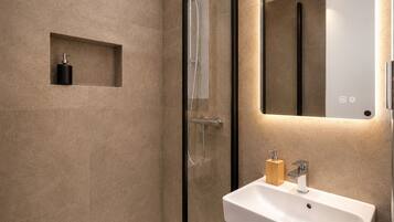 Ein modernes Badezimmer mit einer gläsernen Duschkabine, einem weißen Waschbecken und einer kleinen Holz-Seifenschale.