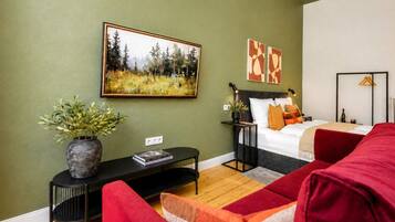 A room with a bed, a desk, a chair, a plant, and artwork on the walls.