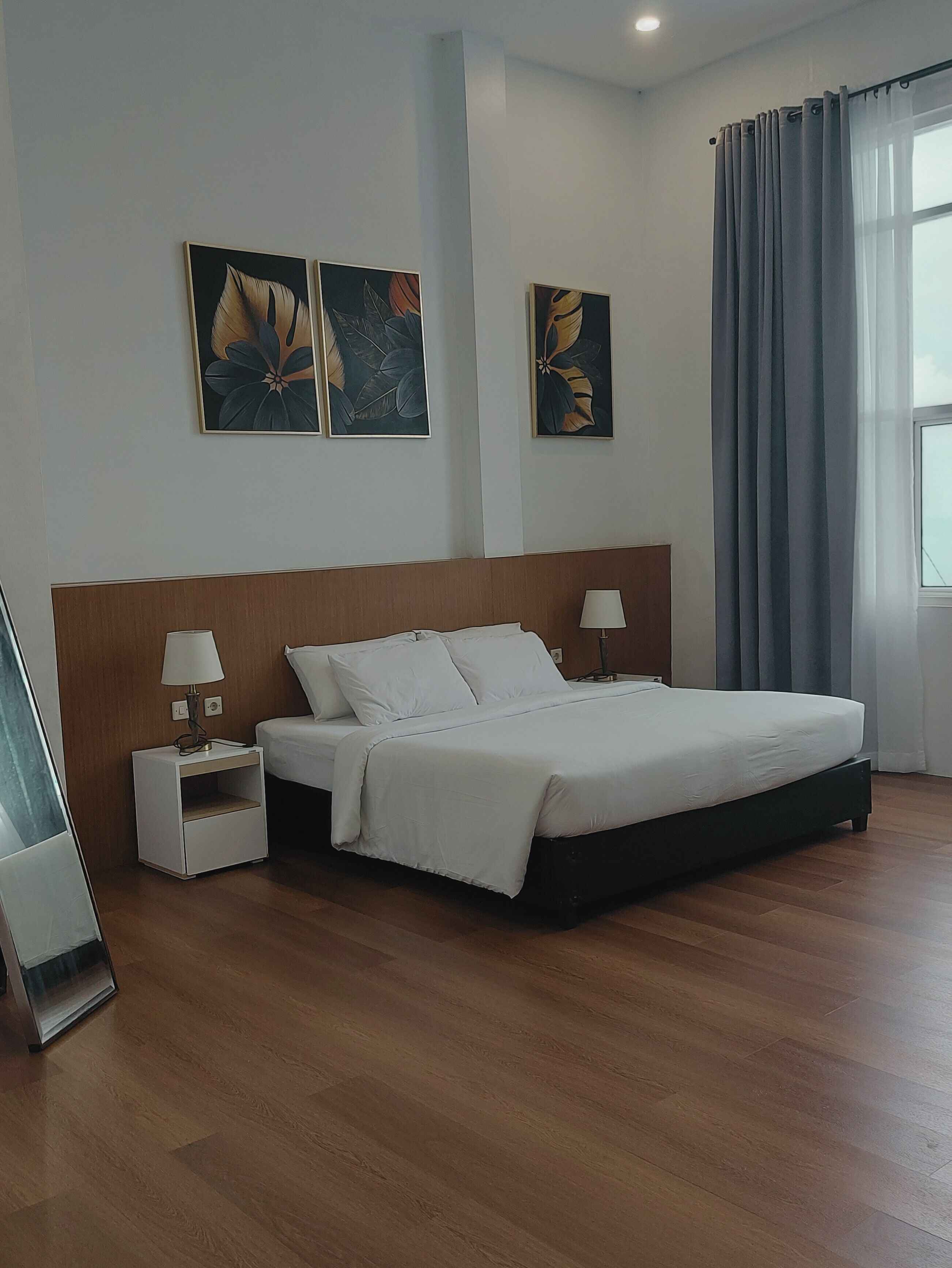 A hotel room with a large bed, two bedside tables with lamps, and three floral artwork on the wall.