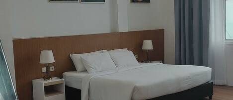 A hotel room with a large bed, two bedside tables with lamps, and three floral artwork on the wall.