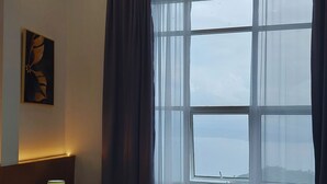 Une chambre d’hôtel avec un lit, une table de chevet avec une lampe, une chaise et une grande fenêtre avec des rideaux.