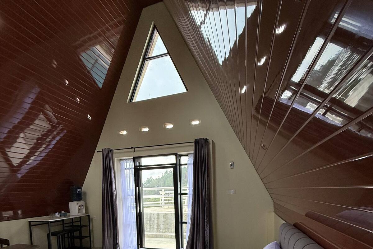 A bedroom with a large bed, a desk, and a view through a glass door.