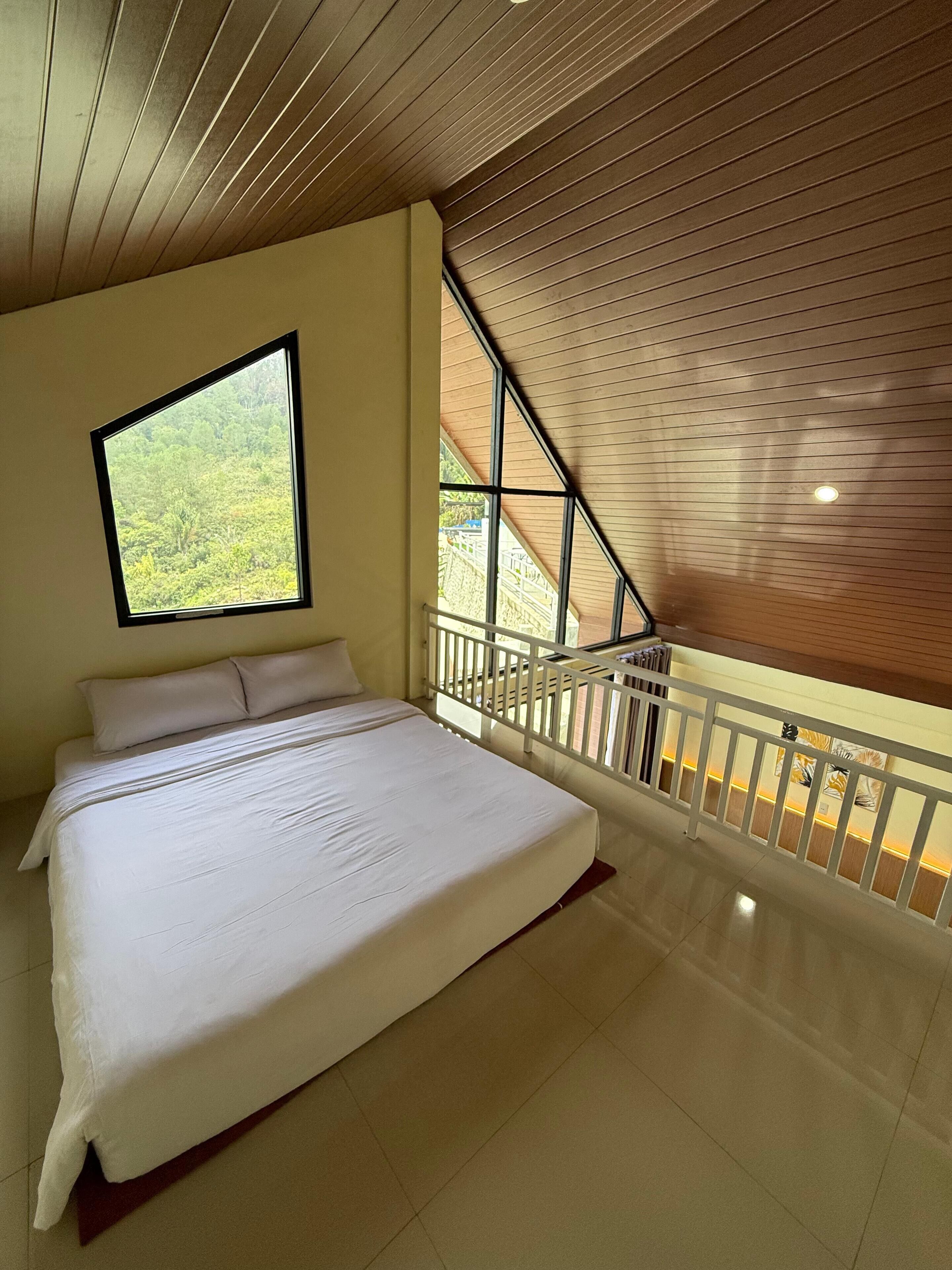 Een slaapkamer met een groot bed, een raam met uitzicht op groen en een balkon met houten hekwerk.
