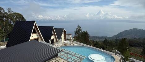 A modern pool area with a glass-enclosed patio, a circular hot tub, and a view of the surrounding landscape.