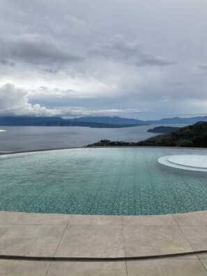 A clear view of a swimming pool with a tiled edge and a view of the surrounding landscape, including distant mountains and a body of water. - Montero Glamping & Stay (Sitanggor)