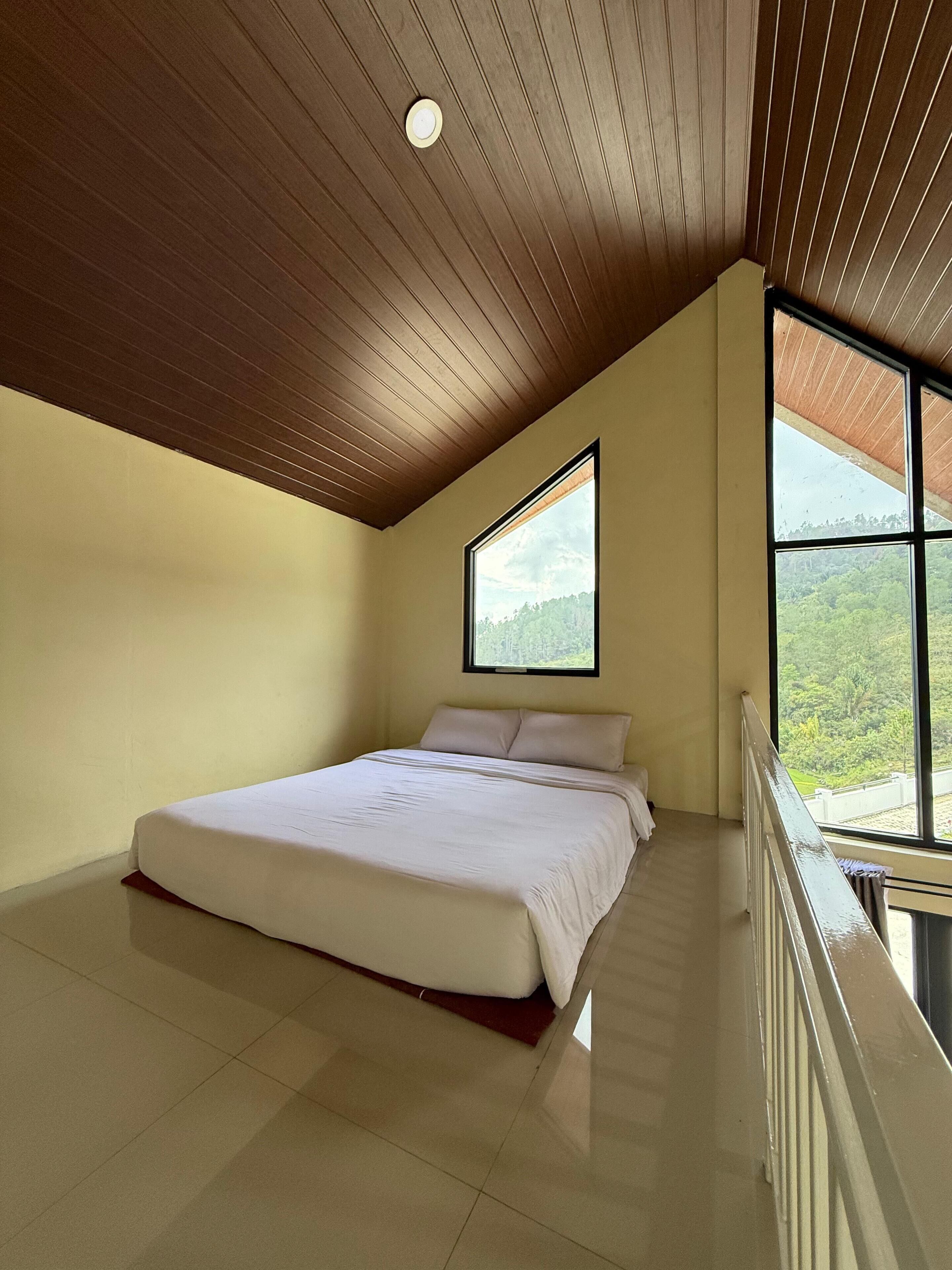 Camera da letto con un letto grande, soffitto in legno e finestra vista verde.