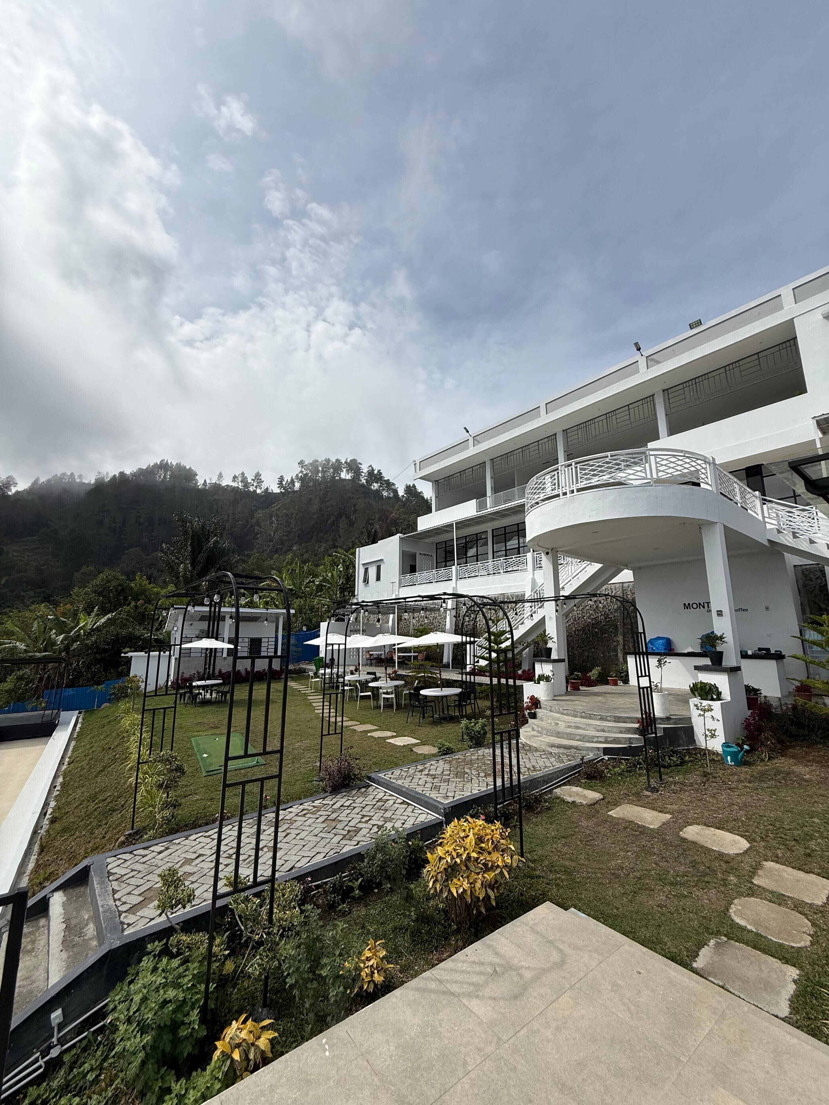 A modern building with a curved balcony, outdoor seating area, and a staircase leading to the entrance.