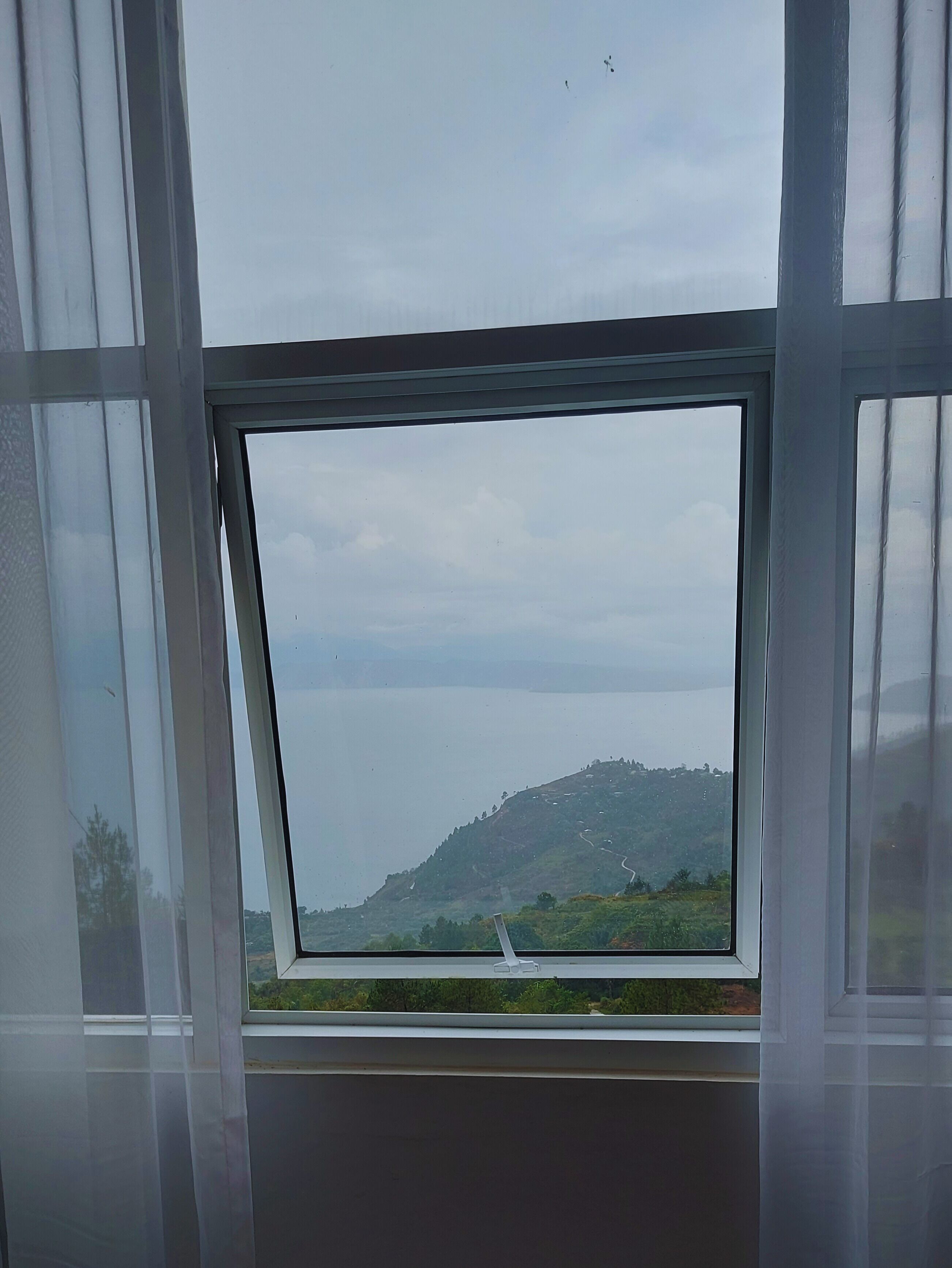 A window with a view of a hilly landscape and a road.