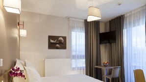 Habitación de hotel con cama, escritorio, silla, televisión y ventana con cortinas.