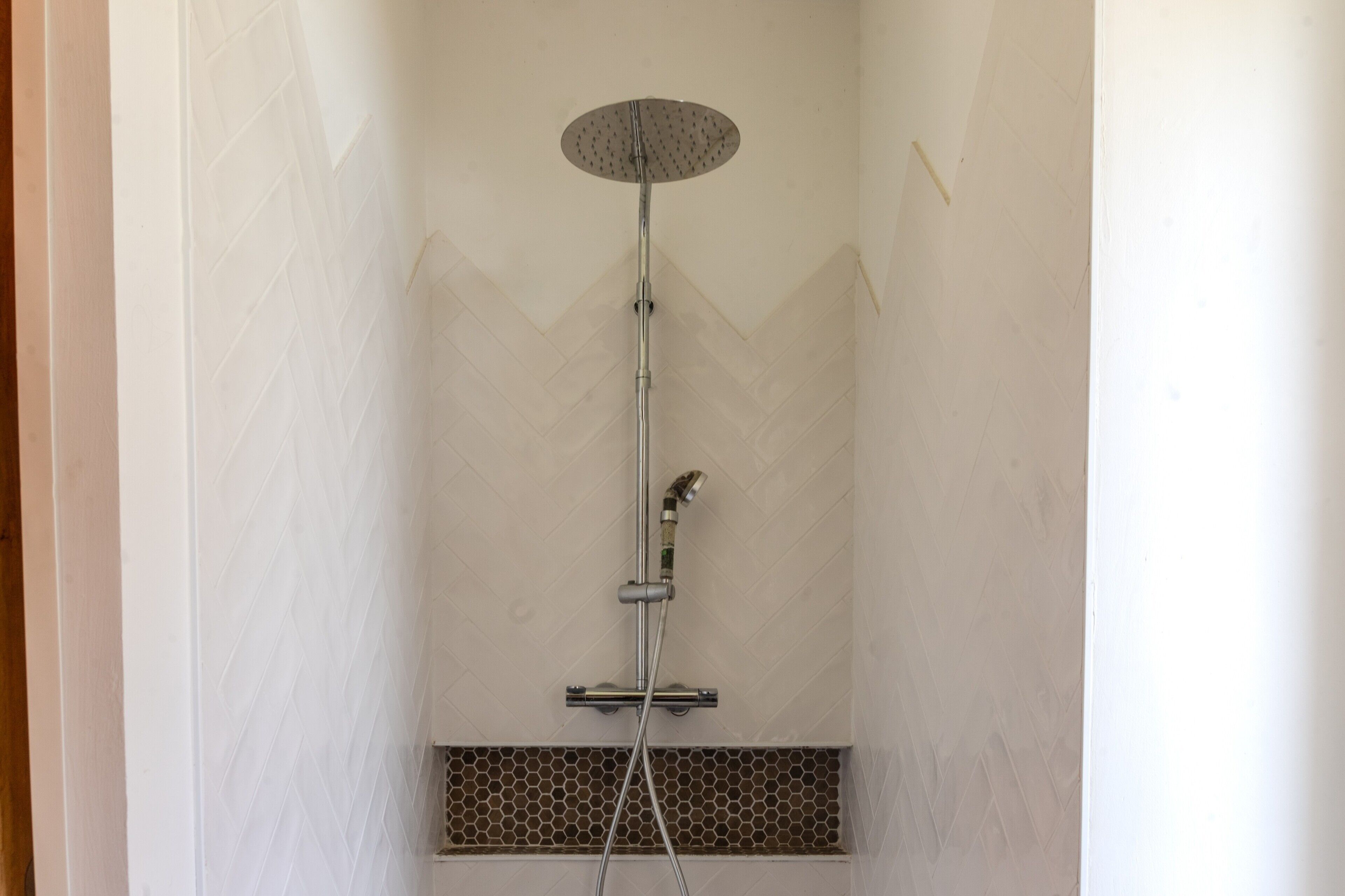 A shower with a rain showerhead, a handheld showerhead, and a handheld showerhead.