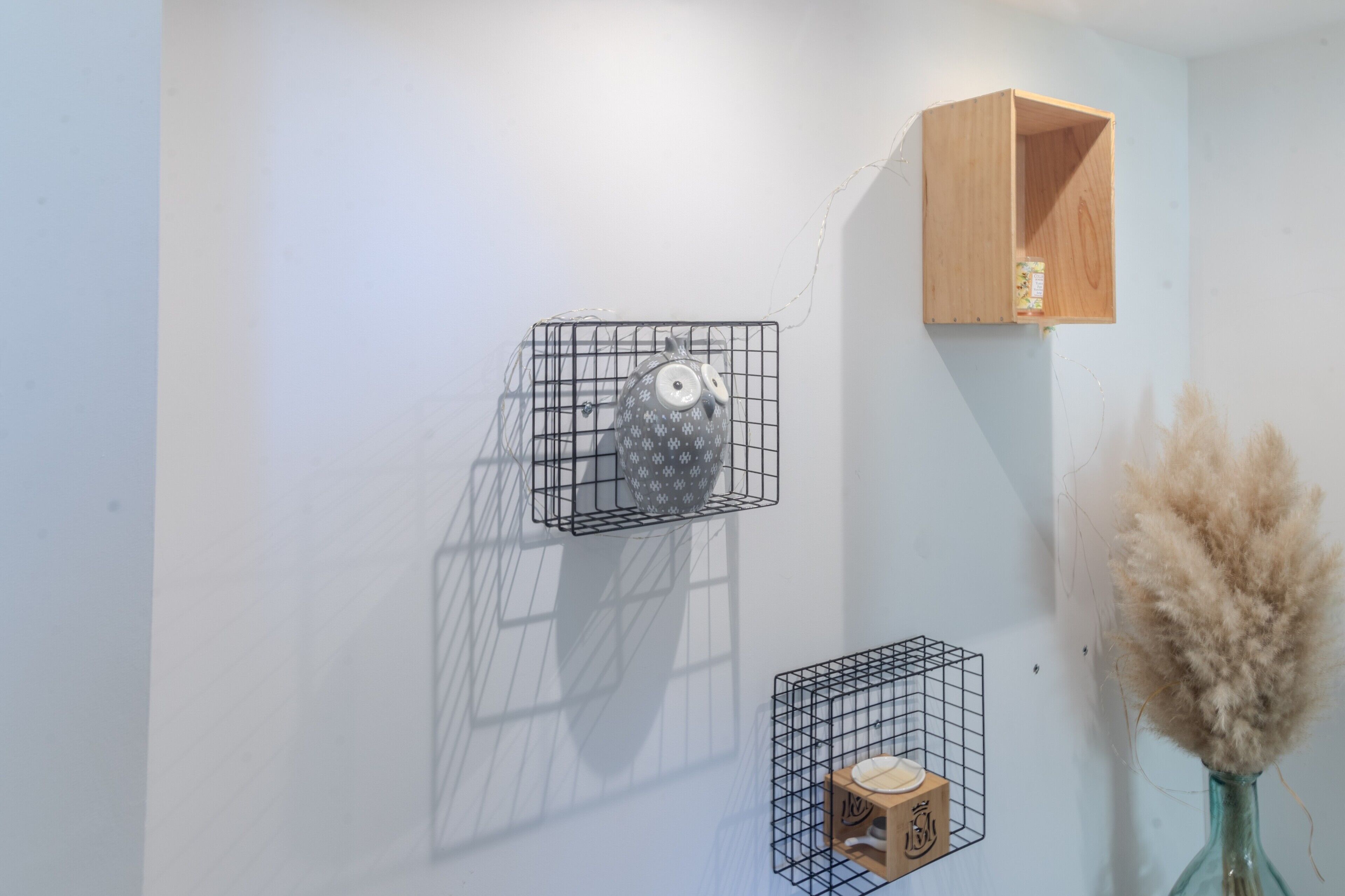 Une pièce avec un mur blanc, une étagère en bois et deux étagères en treillis métallique ornées d’objets décoratifs.