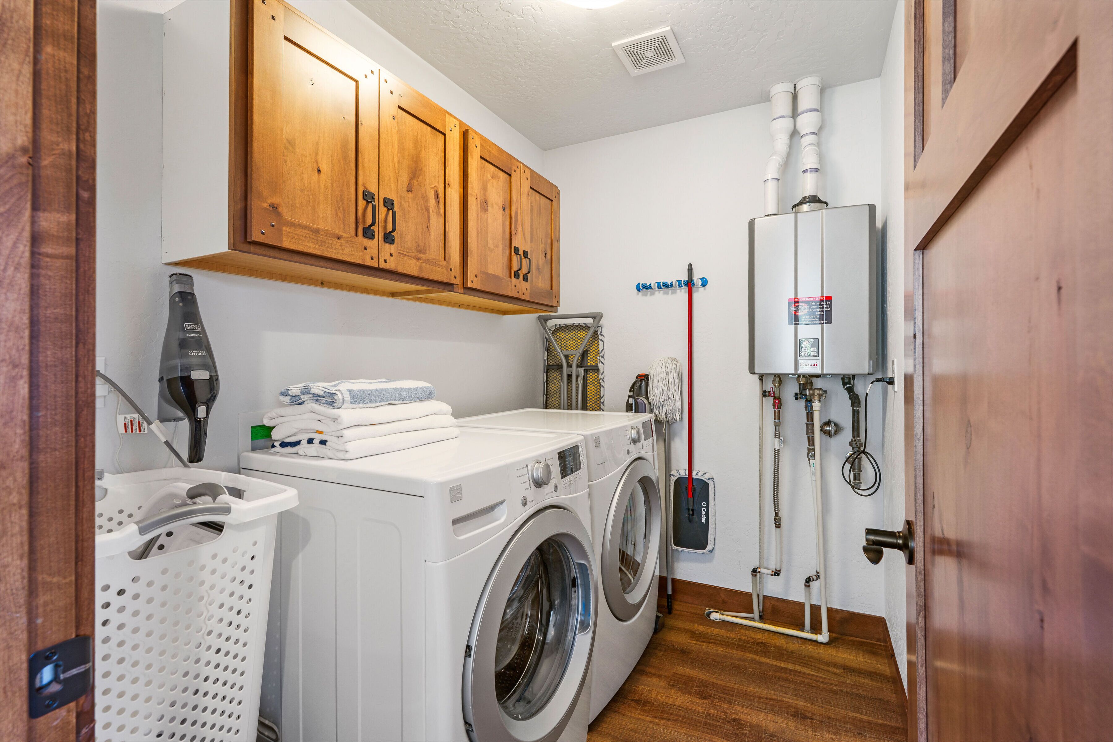 A laundry room with a washing machine, dryer, wooden cabinets, and a water heater.