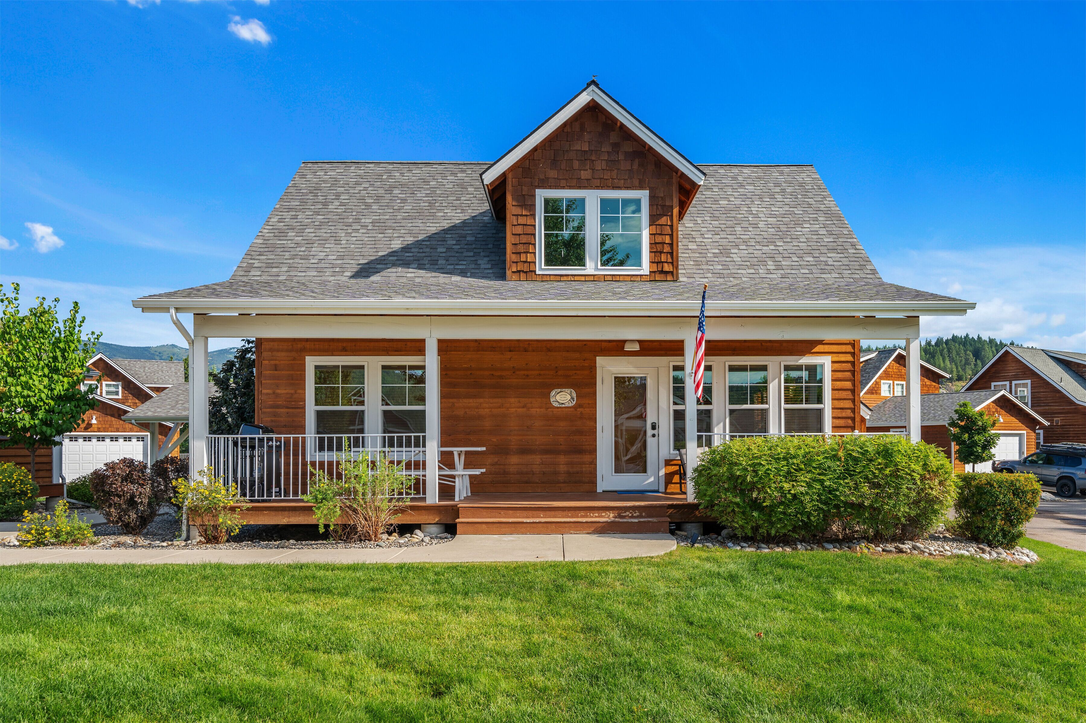 A two-story wooden house with a front porch, a garage, and a well-maintained lawn.