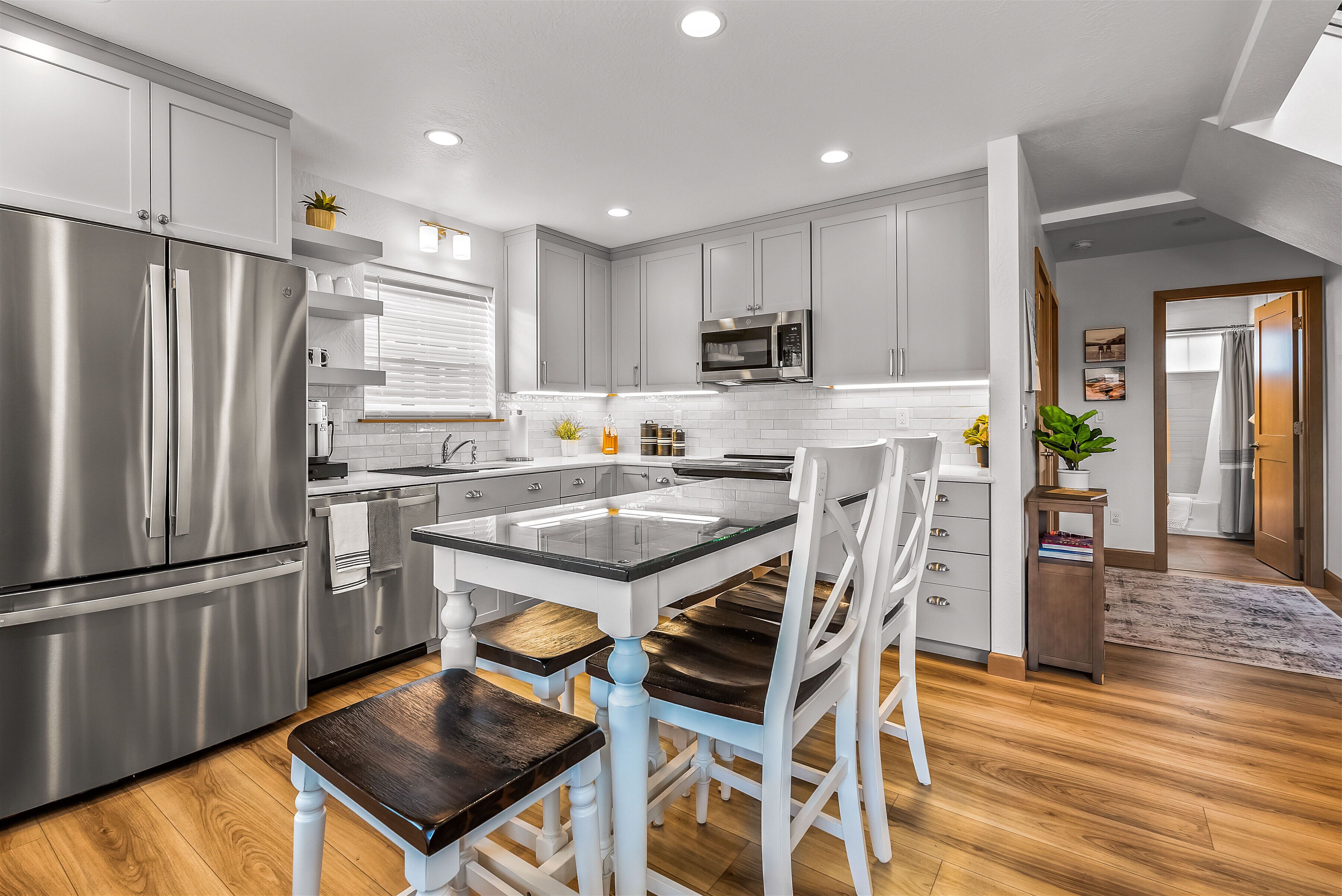 A modern kitchen with stainless steel appliances, white cabinetry, and a central island with chairs.