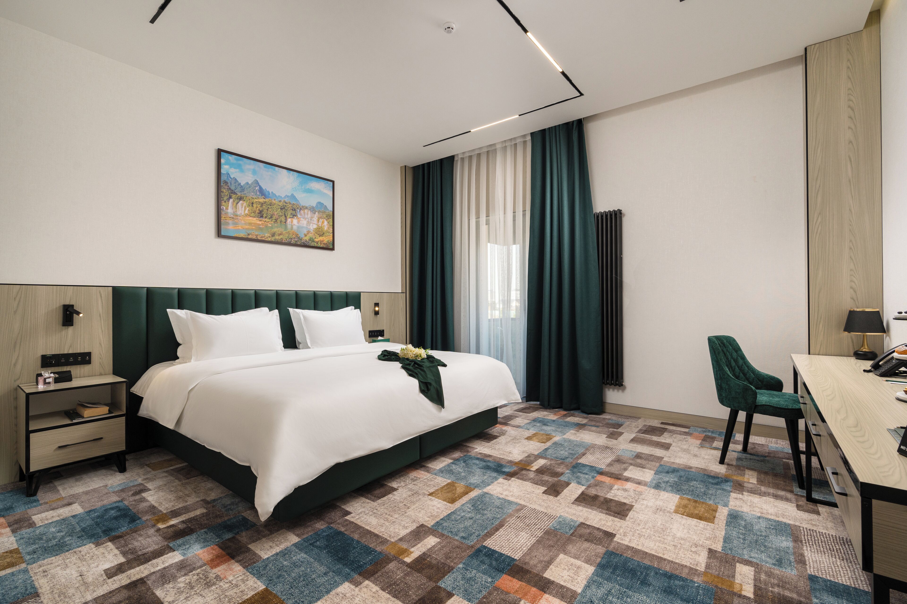 A hotel room with a large bed, a desk, a chair, a nightstand, and a painting on the wall.