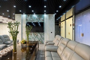 Eine moderne Lobby mit einer Couch, einem Glastisch und einem an der Wand montierten Fernseher.