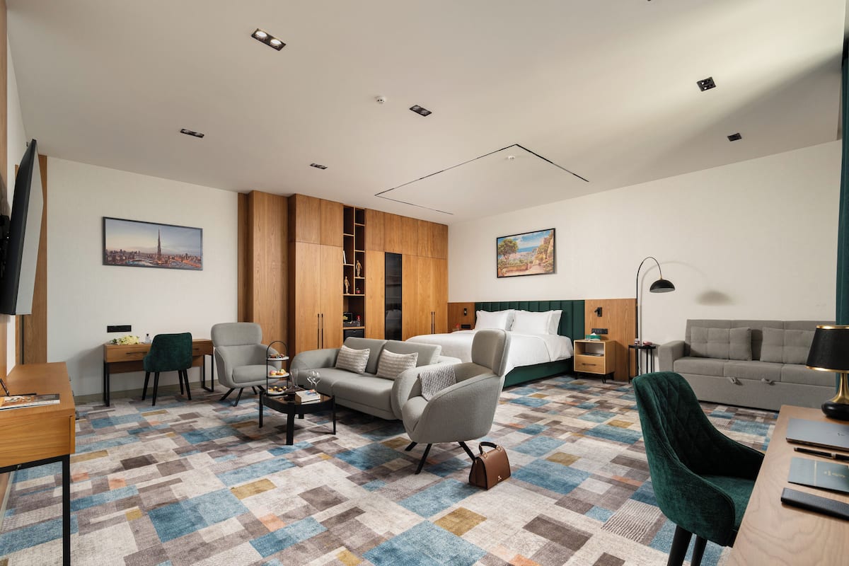 A modern hotel room with a bed, two sofas, a desk, and a TV.